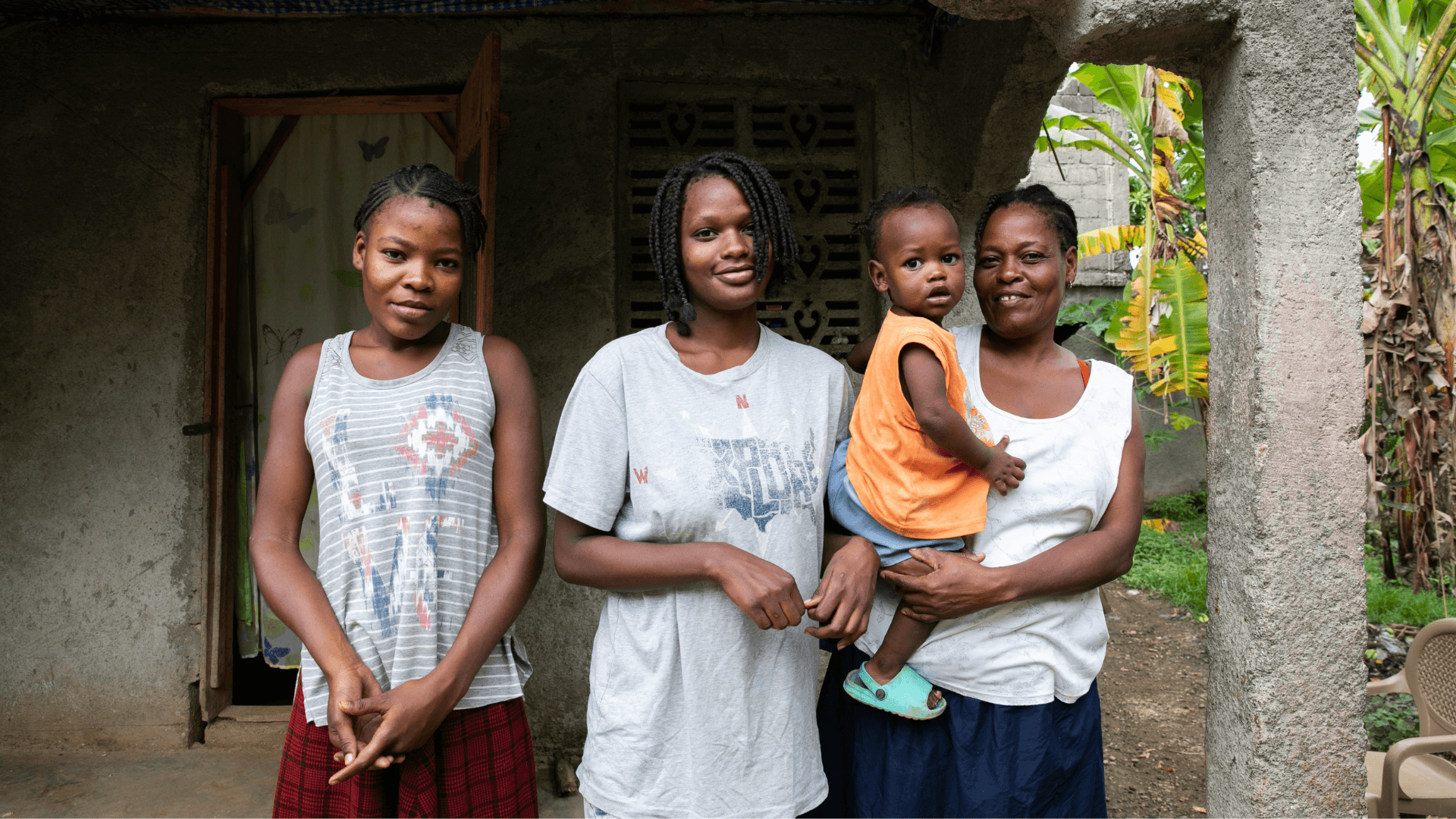 a woman holding a child stands with two girls outside their home in Haiti.