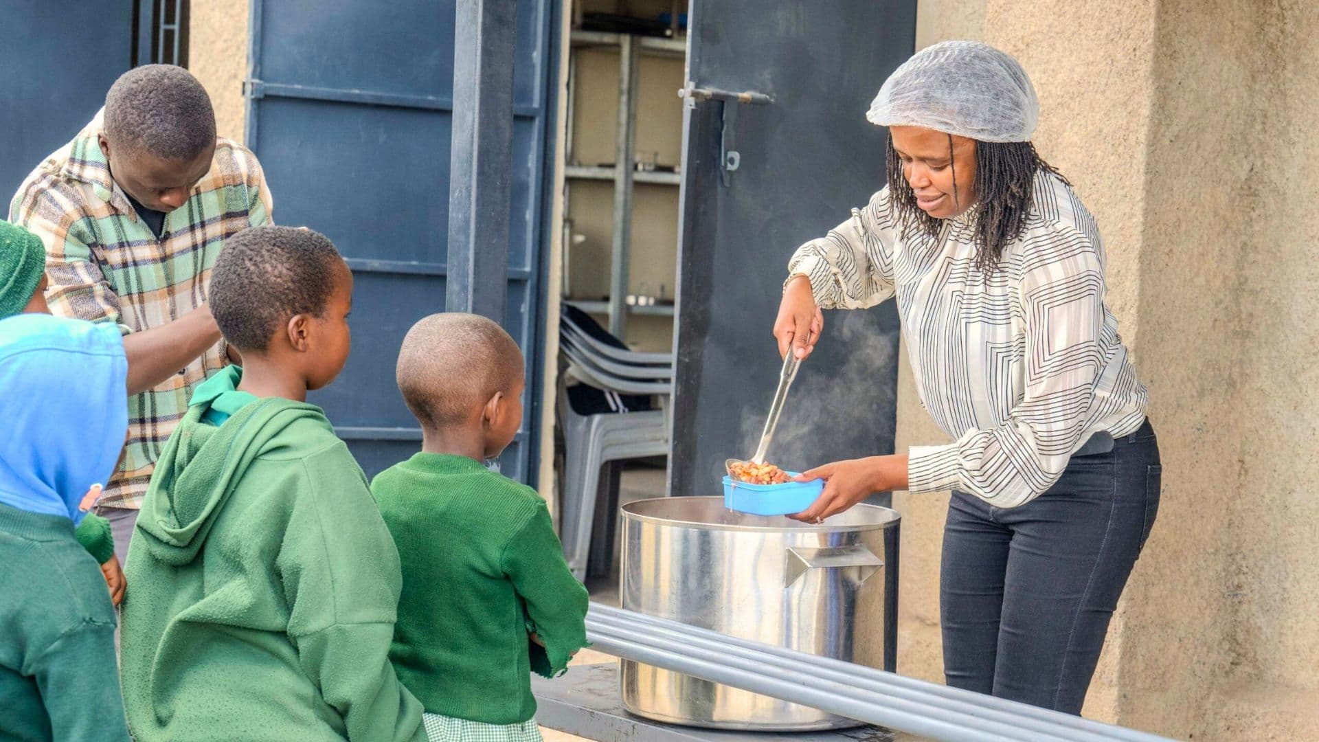 woman serving food to children from a large meal container during a school or community feeding program.