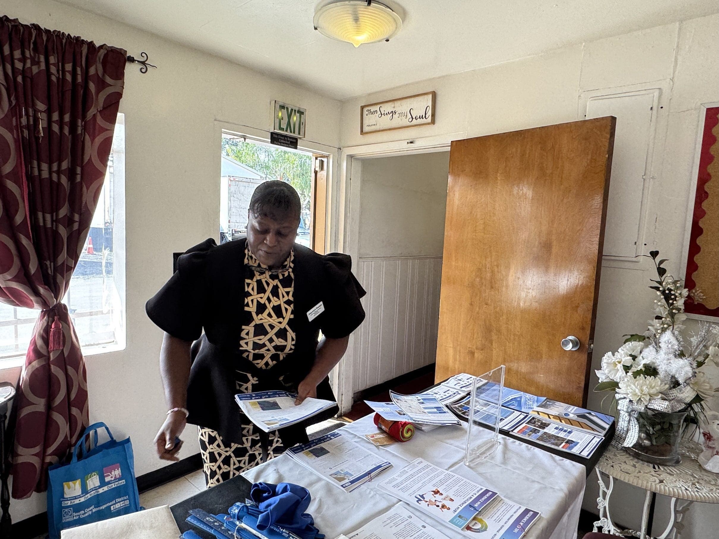 a woman arranges informational brochures and materials on a table inside a community meeting space.