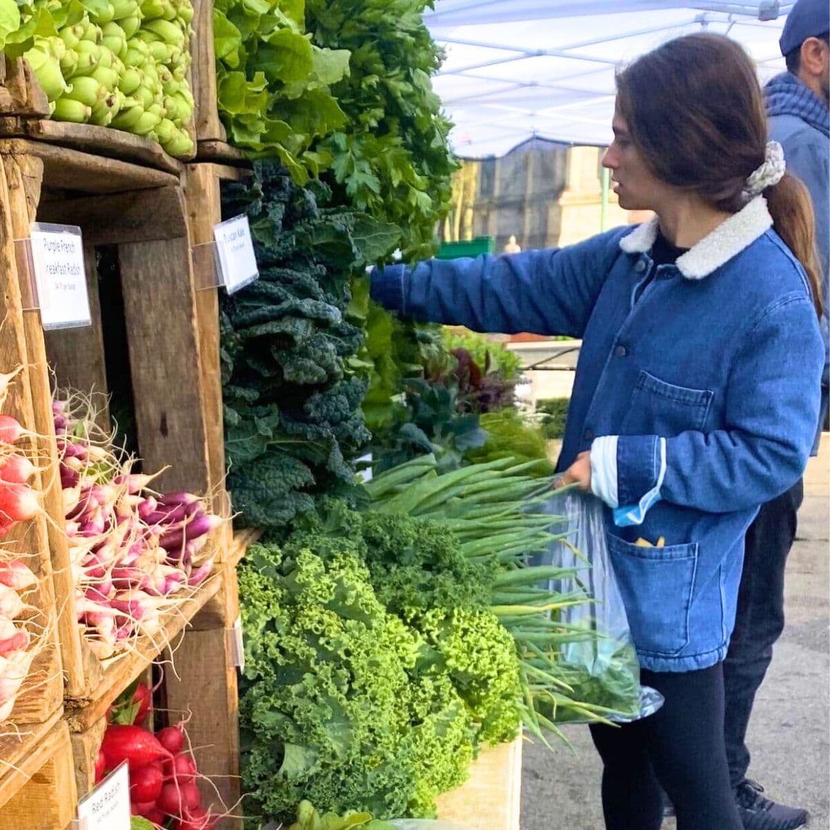 person selecting fresh leafy greens and vegetables at an outdoor farmers market produce stand.