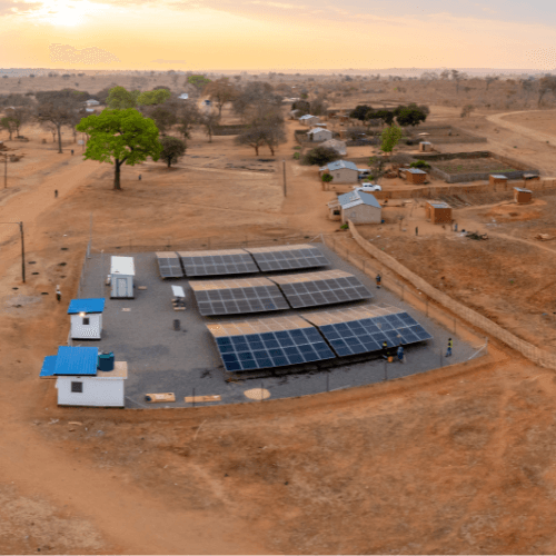 aerial view of a solar energy installation in a rural landscape surrounded by homes and dirt roads.