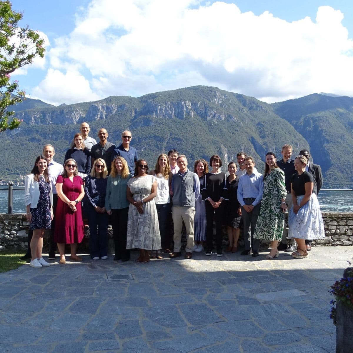 group of professionals posing outdoors by a lakeside terrace with mountains in the background during a gathering at the Bellagio Center.