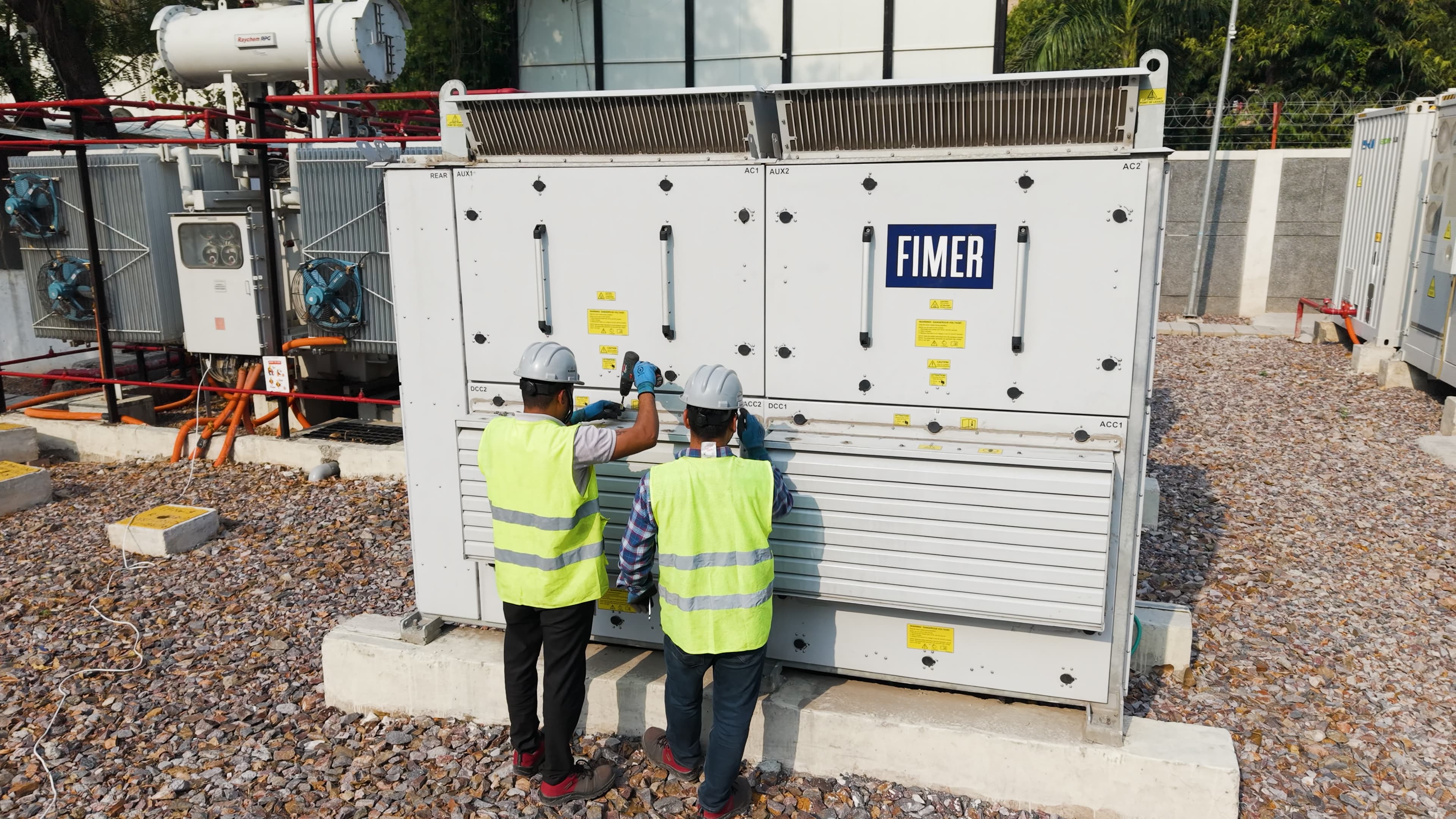 two workers in safety gear service electrical equipment at a battery energy storage facility.